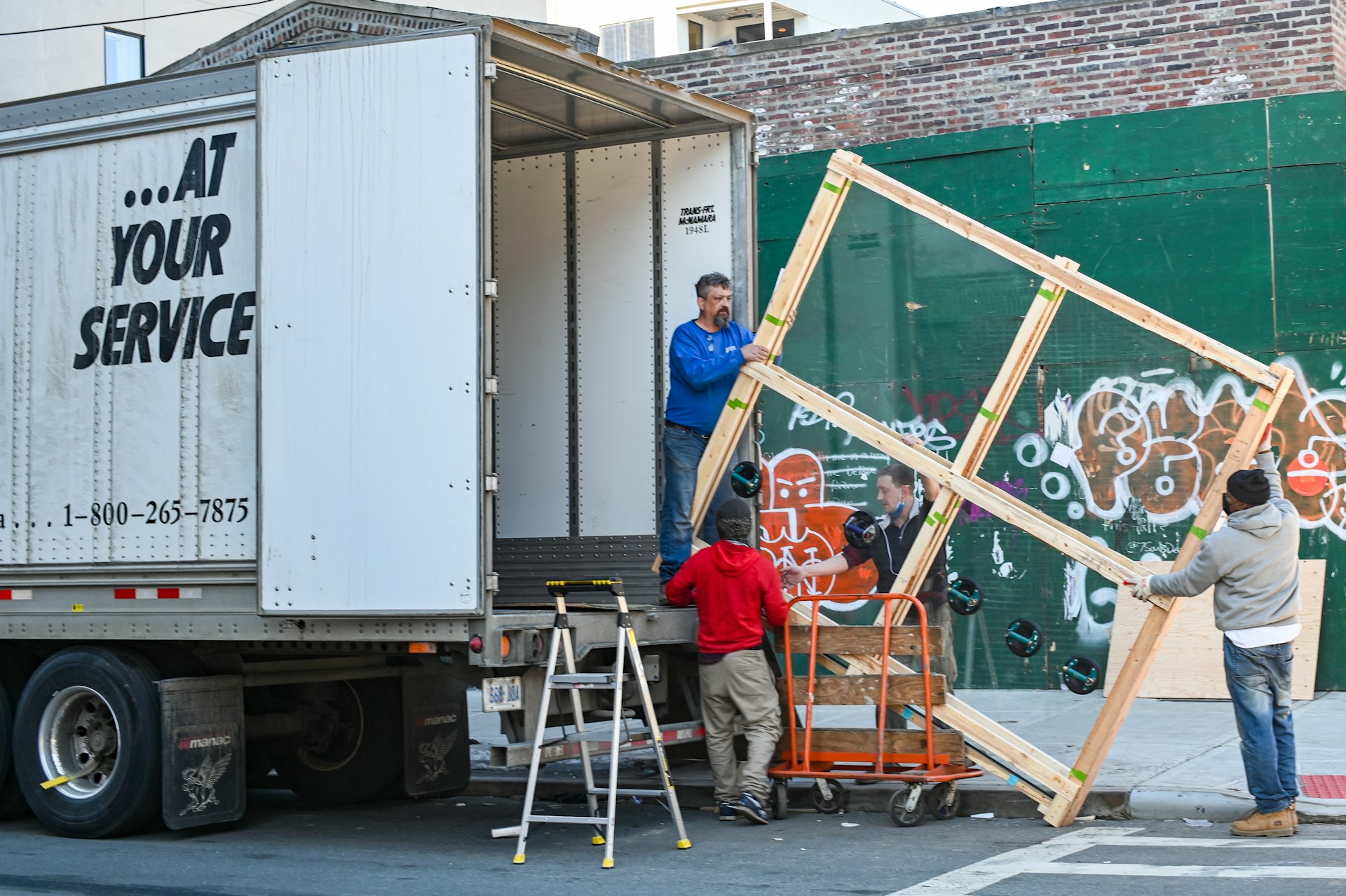 Moving crew loading a large crated frame into a box truck on a city street