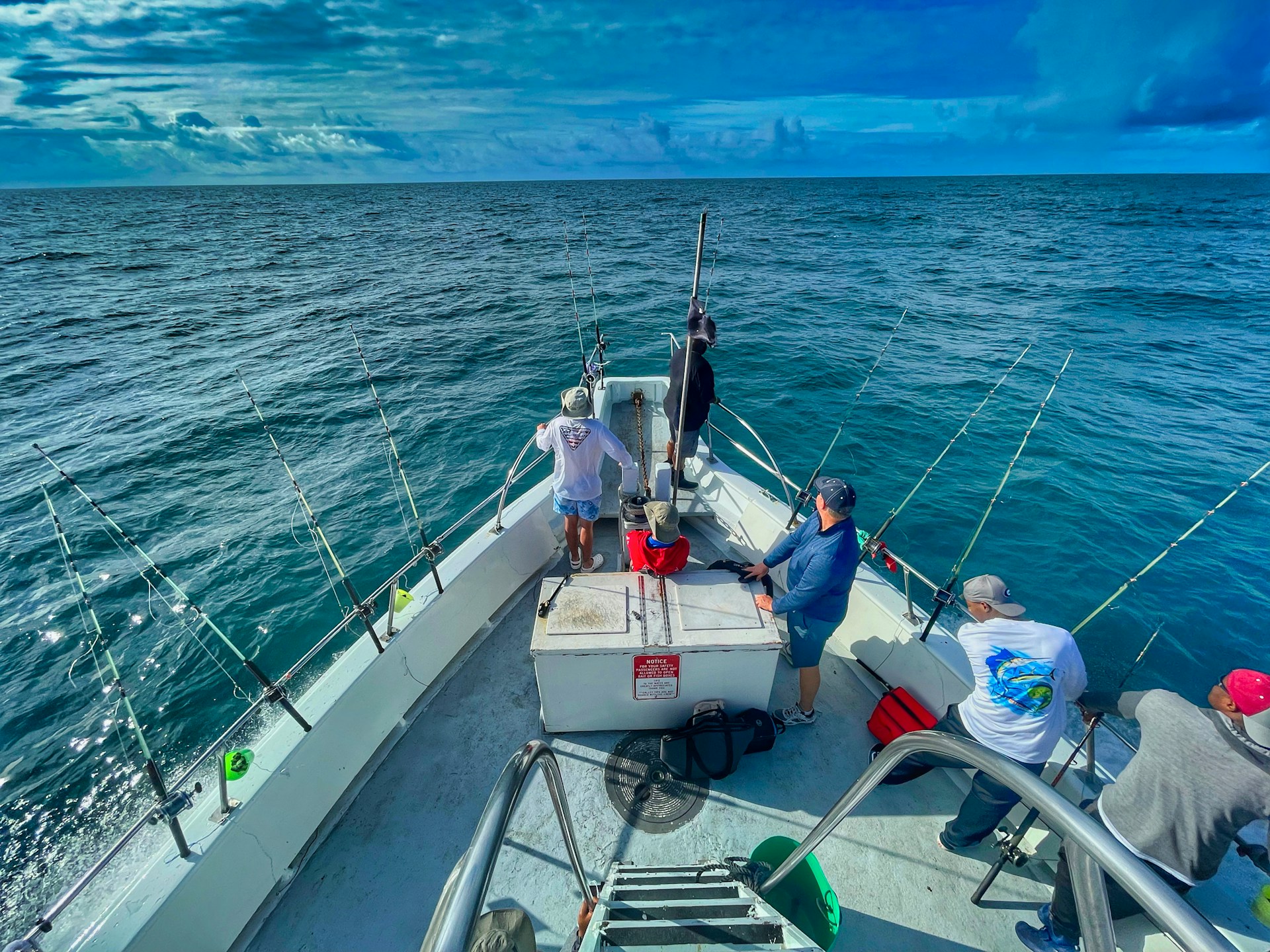Anglers on a charter fishing boat with rods out on open blue water